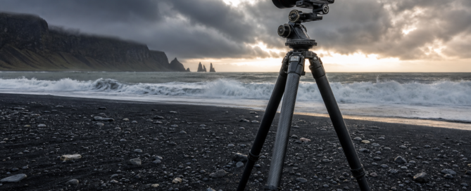 Heavy-duty photography tripod set up on a rugged black sand beach in Iceland under a stormy sky
